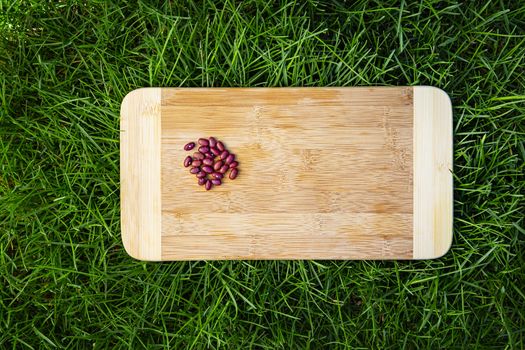 small heap of red kidney bean on top of wood cutting board, sitting on green grass