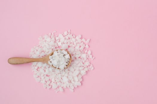 Sea salt in a wooden spoon on pink background for seasoning or preserving food