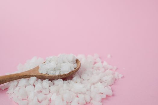 Sea salt in a wooden spoon on pink background for seasoning or preserving food