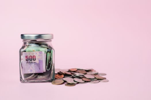 Thai currency banknote and coins in the glass jar on pink background for business, finance, investment and saving money concept