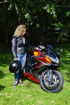 Young blond woman standing beside a sport motorcycle in a park