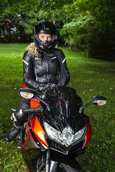 Young woman, in full motorcycle protective gear, sitting on a sport motorcycle