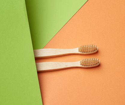 two wooden toothbrushes on a green orange background, plastic rejection concept, zero waste 