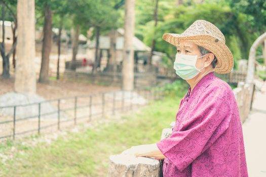 old elder woman wearing facial medical mask resting in garden. asian elderly senior relaxing outdoors. female leisure lifestyle