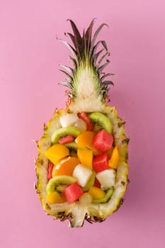 Mix fruit served inside pineapple on pink background