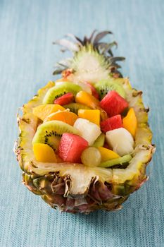 Mix fruit served inside pineapple on blue background