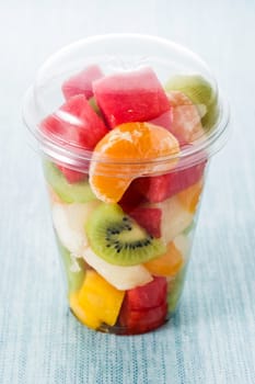 Fresh cut fruit in a plastic cup on blue background