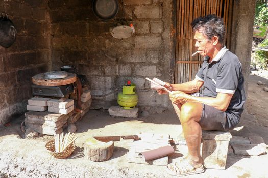 Old man working with bamboo in his workshop to make bamboo straws, Bali, Indonesia. Ecological way of producing recyclable products. Front view to a worker who makes bamboo straws.