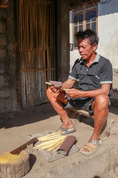 Old man working with bamboo in his workshop to make bamboo straws, Bali, Indonesia. Ecological way of producing recyclable products. Front view to a worker who makes bamboo straws.