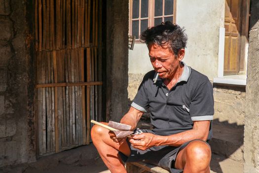 Old man working with bamboo in his workshop to make bamboo straws, Bali, Indonesia. Ecological way of producing recyclable products. Front view to a worker who makes bamboo straws.