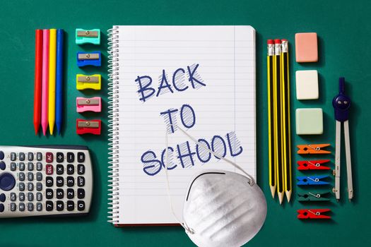 Assortment of school supplies and protective face mask on green background. Back to school concept.