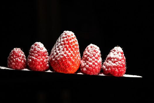 Red Berries balancing on a knife blade with a black background