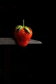 Strawberry balancing on a knife blade with a black background