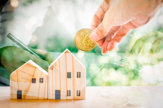 Saving money concept. Double exposure hand hold gloden coin with wooden model home on table with green bokeh background. with businessman. Saving or investment for home in the future.