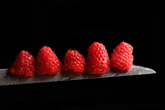 Red Berries balancing on a knife blade with a black background