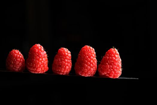 Red Berries balancing on a knife blade with a black background