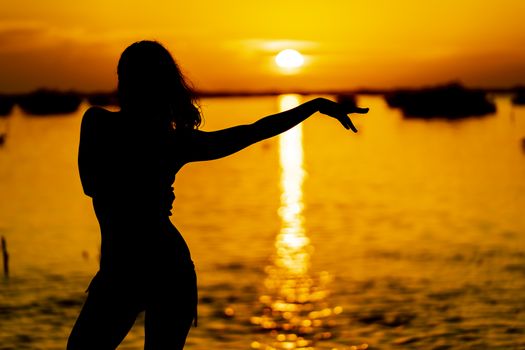 A beautiful latin model is silhouetted as she poses with the rising sun behind her on a exotic Caribbean beach