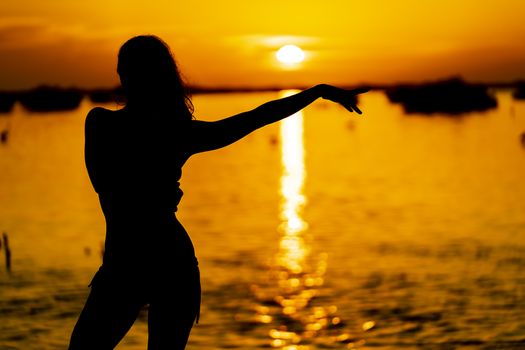 A beautiful latin model is silhouetted as she poses with the rising sun behind her on a exotic Caribbean beach