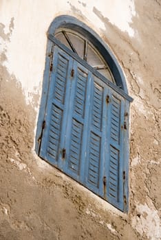Essaouria, Morocco - September 2017: Angled faded blue shuttered window with fanlight set in a peeling plaster wall  - dutch tilt
