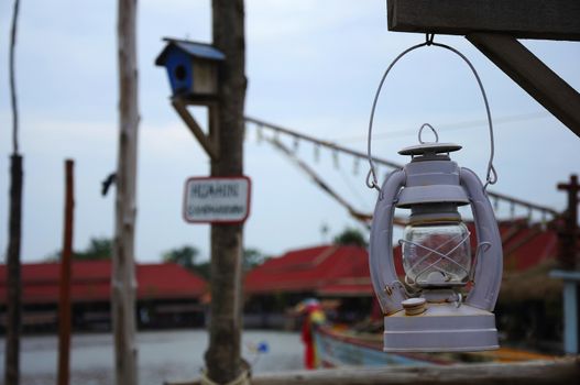 A gray oil lamp hanging under a wooden beam, On a blureed background.