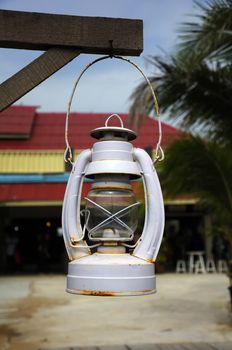 A gray oil lamp hanging under a wooden beam, On a blureed background.