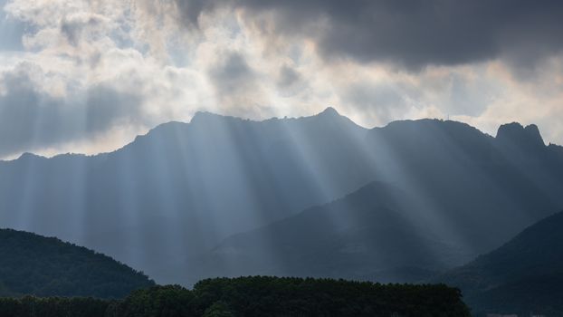Bright sunlight shining through hole of clouds to dark scene of mountain range in Spain