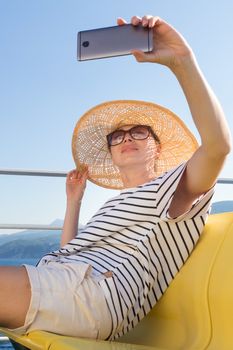 Beautiful, romantic blonde woman taking selfie self portrait on summer vacations traveling by cruse ship ferry boat. Summer vacation lifestyle.