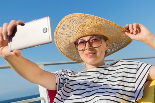 Beautiful, romantic blonde woman taking selfie self portrait on summer vacations traveling by cruse ship ferry boat. Summer vacation lifestyle.