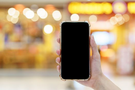 Mockup, hands holding blank black screen mobile phone in blurred department store, digital payment concept