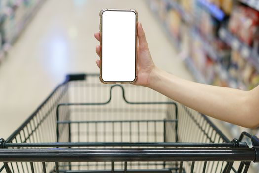 Mockup, hands holding blank white screen mobile phone with shopping cart in supermarket, digital payment concept