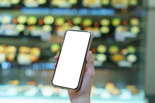 Mockup, hands holding blank white screen mobile phone in blurred food display, digital payment concept