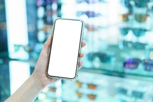 Mockup, hands holding blank white screen mobile phone in blurred glasses shop, digital payment concept