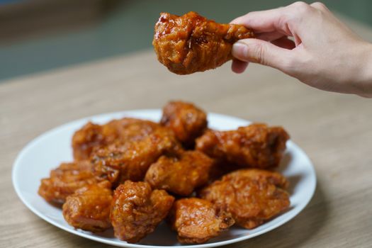 Hand holding spicy deep fried chicken wings, Korean food style.