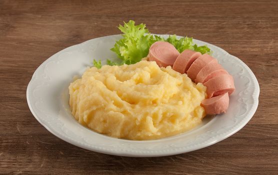 White plate with mashed potatoes, boiled small sausage and fresh green lettuce on the wooden table