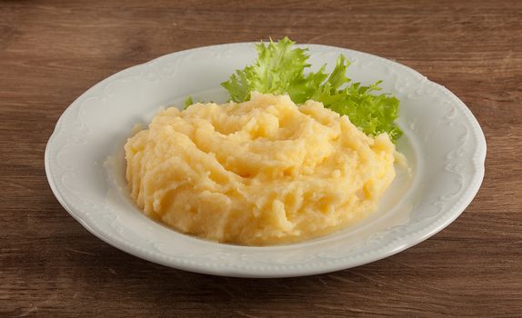 White plate with mashed potatoes nd fresh green lettuce on the wooden table