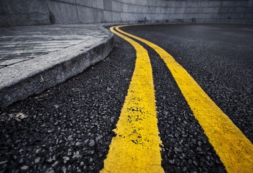 Detail of curved double yellow line on black asphalt painted along curb