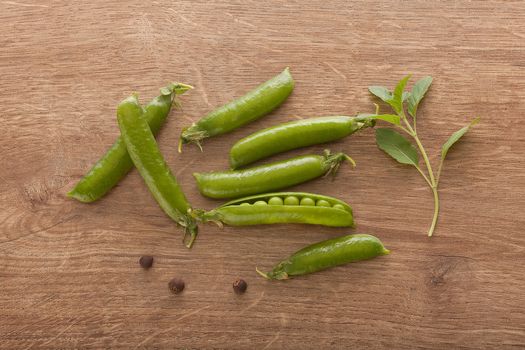 Top view of fresh green pea pods and branch of basil on the wooden table