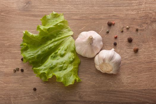 Top view of two head of garlic, fresh green lettuce and black pepper on the wooden table
