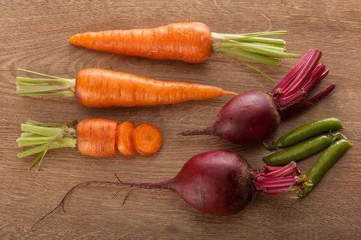 Top view of whole and sliced carrots, beets and fresh green pea pods on the wooden table