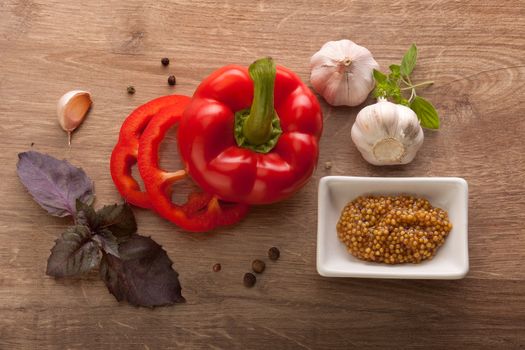 Top view of red paprika, heads and clove of garlic, purple basil, black pepper and grainy mustard on the wooden table