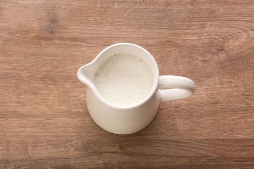 Top view of white pitcher with milk on the wooden table