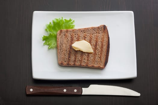 Top view of toasted rye bread with butter and lettuce on the white plate