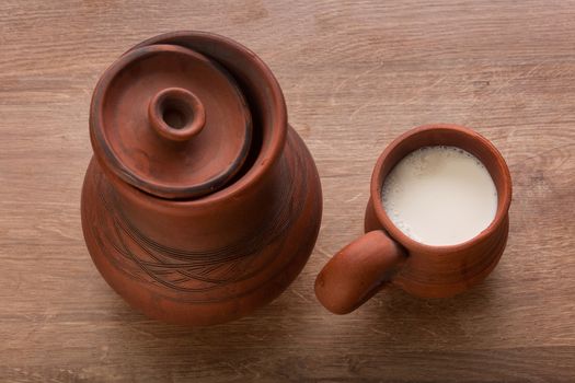 Top view of clay jug and mug with milk on the wooden table