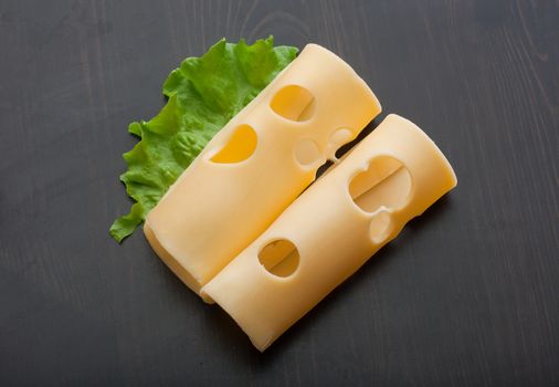 Top view of two rolled pieces of maasdam cheese and green lettuce on the black wooden table