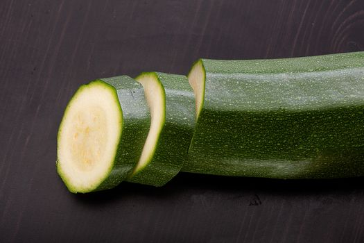 Top view of slices of green zucchini on the black wooden table