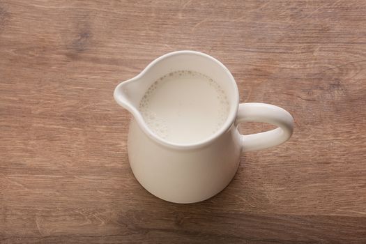 Top view of white pitcher with milk on the wooden table