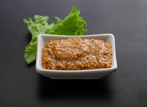 Grainy mustard in the white plate and fresh lettuce on the black wooden plate