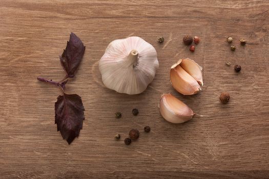 Top view of head and cloves of garlic, purple basil and black pepper on the wooden table