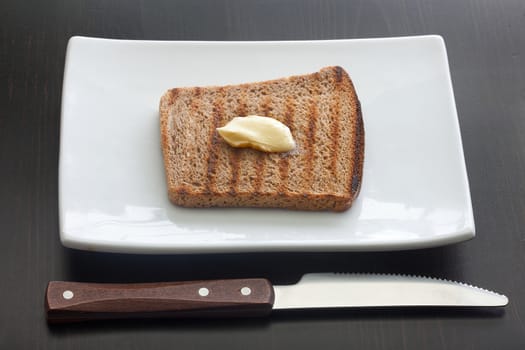 Top view of toasted rye bread with butter on the white plate