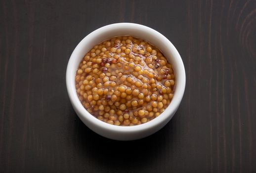 Top view of white plate with grainy mustard on the black wooden table